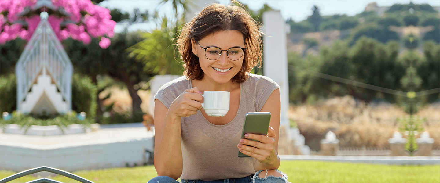 Frau die Kaffee trinkt und lächelnd auf ihr Smartphone blickt.