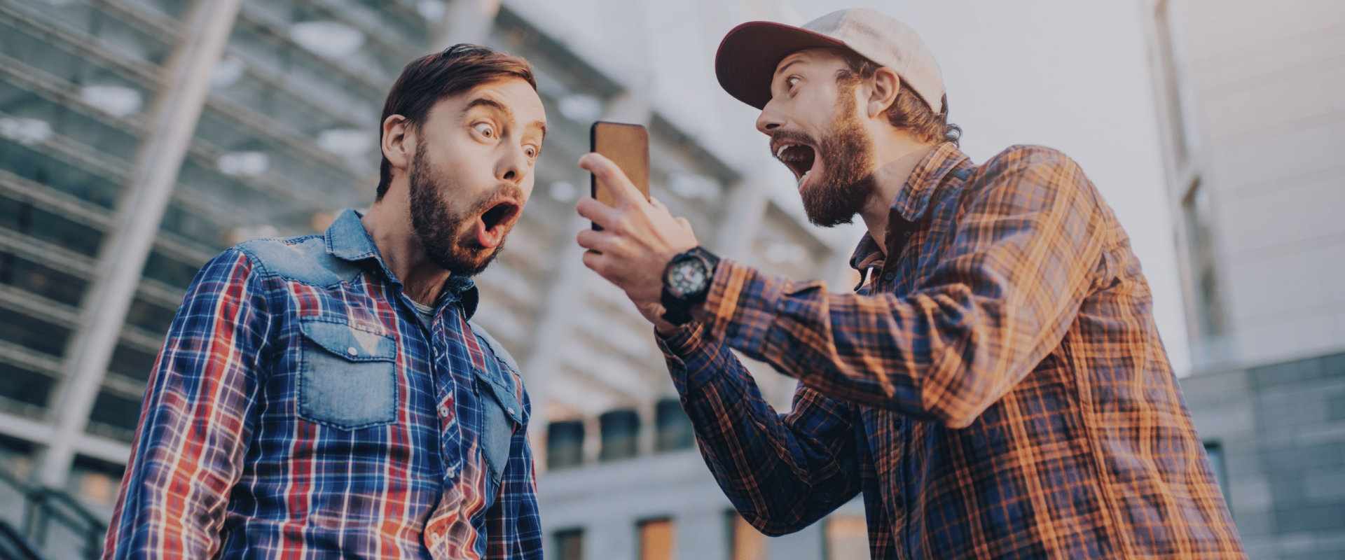 Zwei Freunde die auf ein Smartphone blicken und lustig lachen